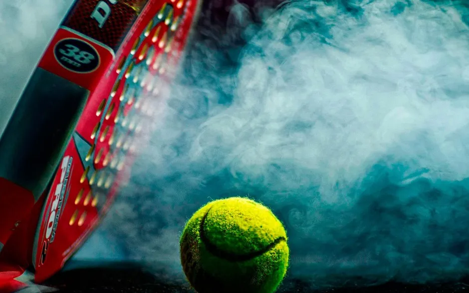 Pala de pádel y pelota sobre la pista, iluminadas entre el humo de los focos.
